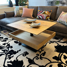 Laden Sie das Bild in den Galerie-Viewer, Höhenverstellbarer Couchtisch Ronald Schmitt Lignum K472 mit offener Ablage und verschiebbarer Schublade aus massiver gerillter Eiche, inszeniert in moderner Wohnzimmerumgebung.