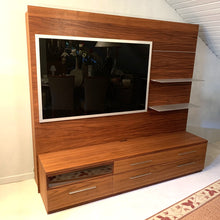 Laden Sie das Bild in den Galerie-Viewer, Moderne Wohnwand Amar aus Nussbaum von AERA Design – schräge Perspektive mit TV-Paneel und Regalstruktur.