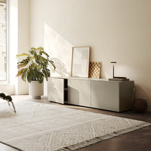 Laden Sie das Bild in den Galerie-Viewer, Piure Nex Pur Box 2020600 in Silk in heller Wohnumgebung – 3-türiges Sideboard unter Fenster, dekorativ inszeniert mit Kunst, Lampe und Pflanzen.