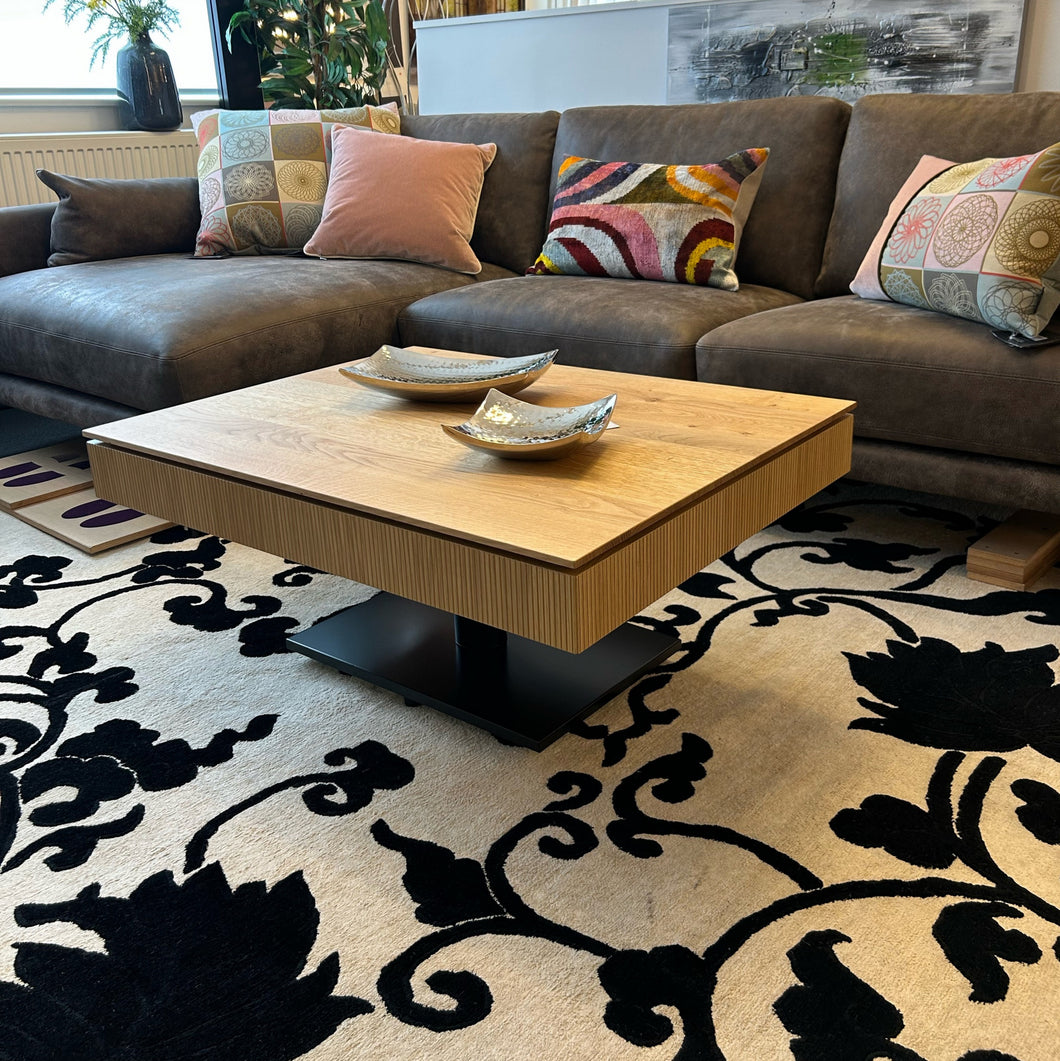 Design-Couchtisch Ronald Schmitt Janus K472 Lignum mit massiver Schublade in Wildeiche natur und vertikaler Rillenstruktur – geschlossen im Wohnambiente mit Ecksofa und Teppich.