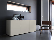 Laden Sie das Bild in den Galerie-Viewer, Elegantes Sideboard Piure 2020500 in Farbe Silk, modern inszeniert vor dunkler Wand mit Skulpturen und Vasen
