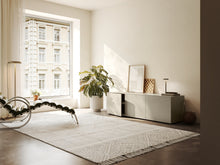 Laden Sie das Bild in den Galerie-Viewer, Piure Nex Pur Box 2020600 in Silk in heller Wohnumgebung – 3-türiges Sideboard unter Fenster, dekorativ inszeniert mit Kunst, Lampe und Pflanzen.
