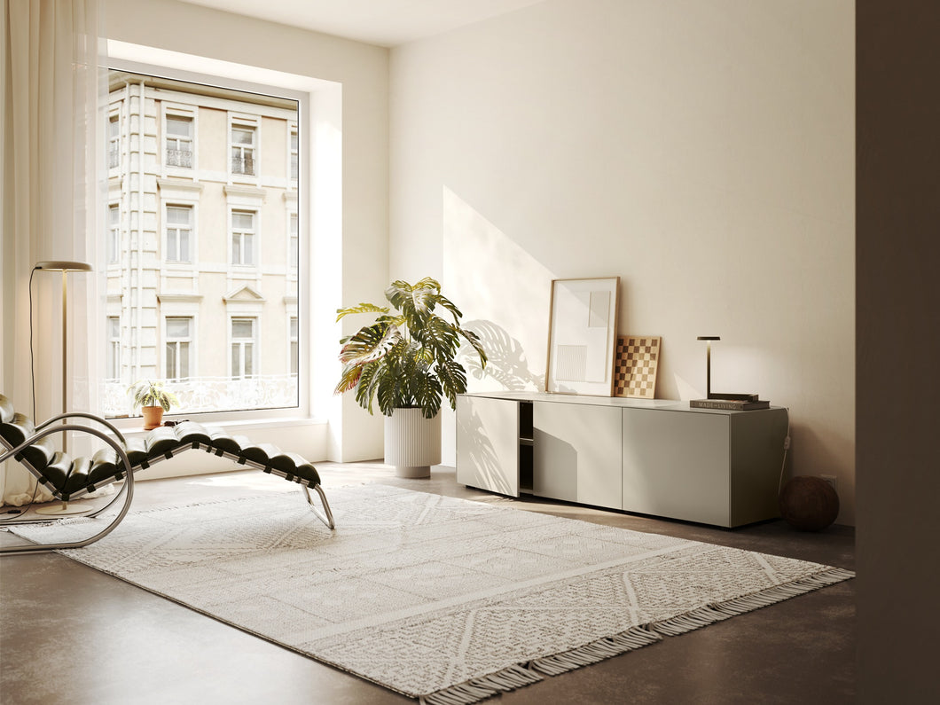 Piure Nex Pur Box 2020600 in Silk in heller Wohnumgebung – 3-türiges Sideboard unter Fenster, dekorativ inszeniert mit Kunst, Lampe und Pflanzen.