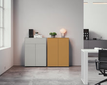 Laden Sie das Bild in den Galerie-Viewer, Design-Kombination aus Piure Nex Pur Box 2041100 in Cool Grey und 2041300 in warmem Hazelton – stilvoll arrangiert in einem hellen, zeitgenössischen Arbeitsbereich mit wohnlichem Flair.
