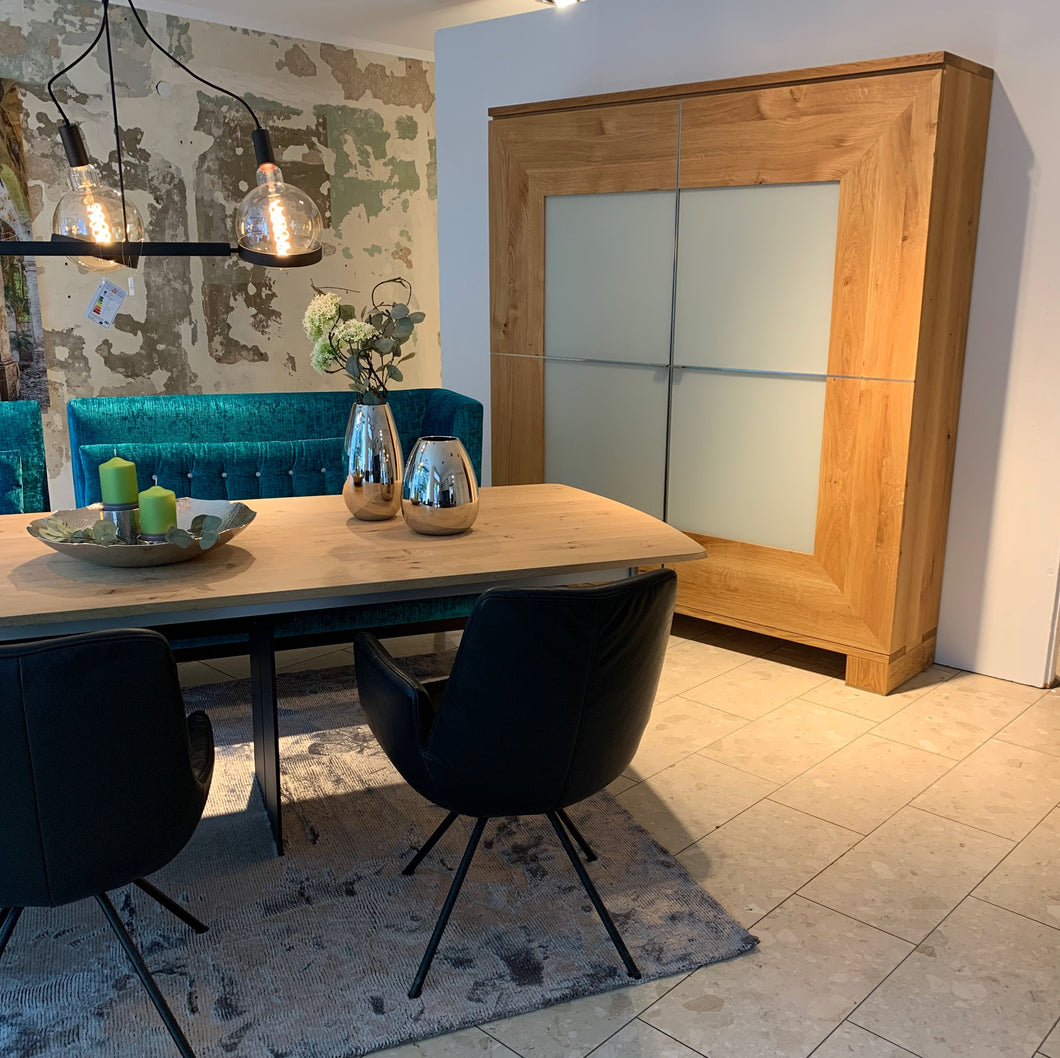 Großer Schrank Varus von Scholtissek in knorriger Eiche mit Glasfront in Sand matt – inszeniert im Essbereich mit Designmöbeln