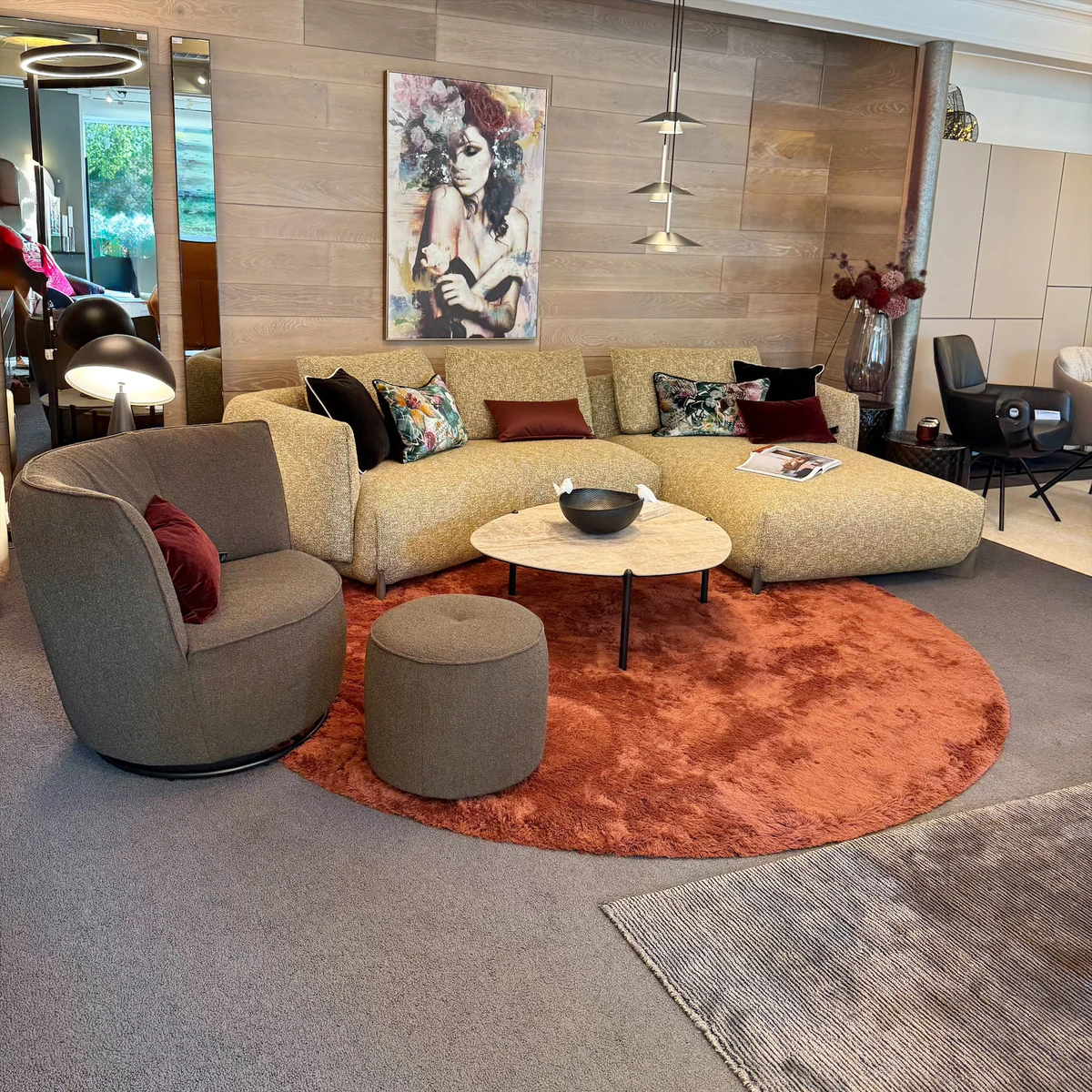 Wohnbereich mit Ecksofa, rundem Sessel und rostfarbenem Teppich in der Ausstellung Zeppenfeld